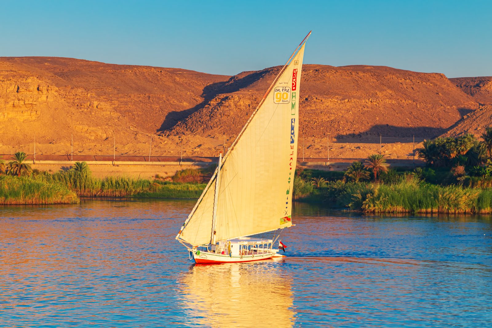 فلوكة بشراعها الذهبي على النيل أمام كثبان أسوان
